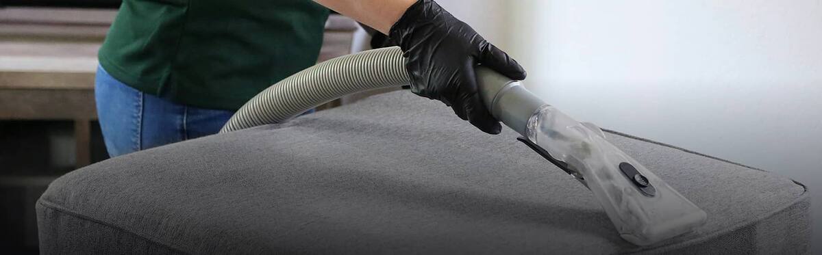 Gloved hand vacuuming a grey fabric lounge